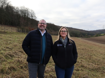 A man (Nick Smith - left) and woman (Debbie Tann MBE - right) stand posing for a photo on a sloped field 