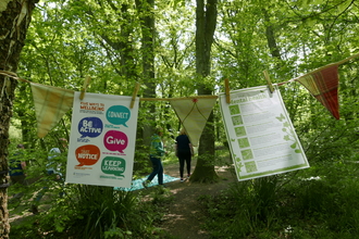 2 nature wellbeing posters explaining how to connect to nature hanging on some bunting out in a green woodland area