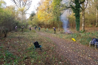 Several volunteers carrying out conservation tasks in the background. A small bonfire burns on the right