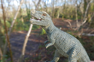 A toy dinosaur in the woods.