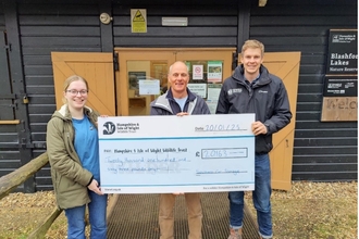 three people standing in front of a wooden building holding a large cheque for £2016