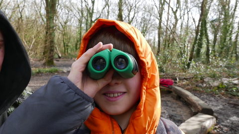 Boy looking through binoculars in a woodland.