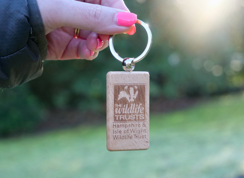 hand holding keyring over green nature background. keyring features HIWWT logo