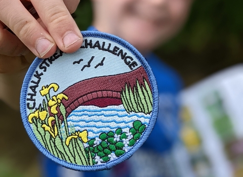 Child holding a Chalk Stream Challenge badge © Katy Seaman